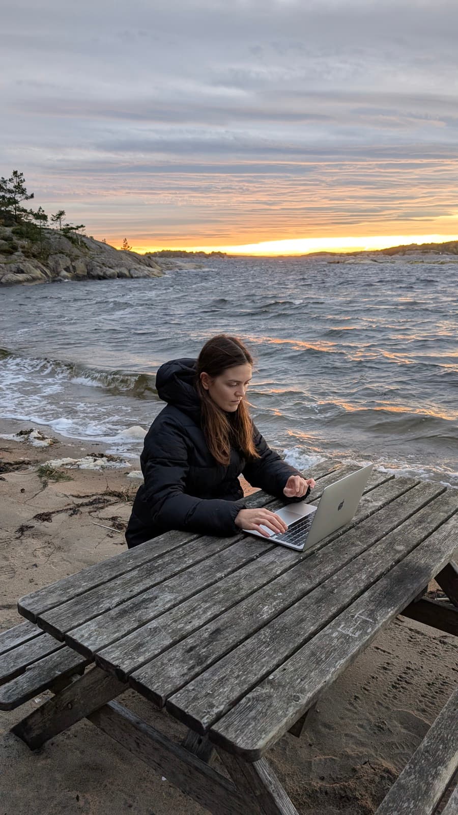Natallia working on a laptop at a seaside picnic table at sunset