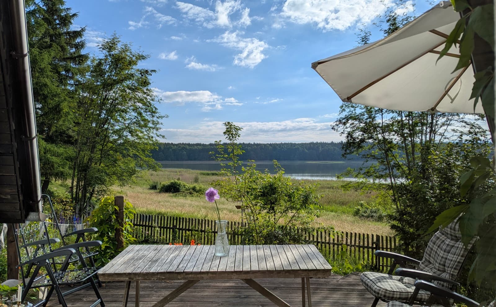 A sunlit terrace with a table and a lake view at one of our European house sits