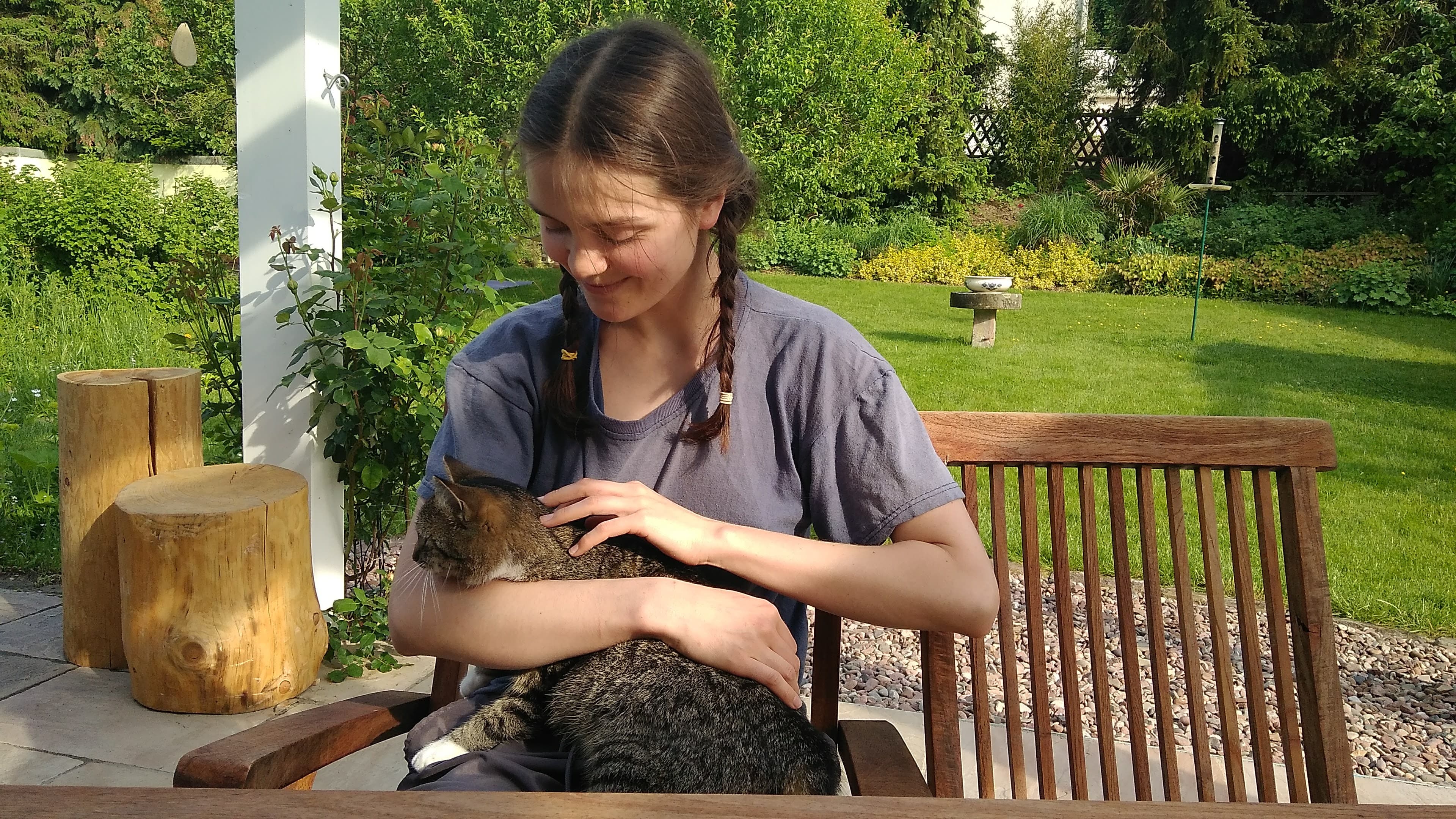 A pet sitter relaxing in a sunny garden with a cat curled on her lap